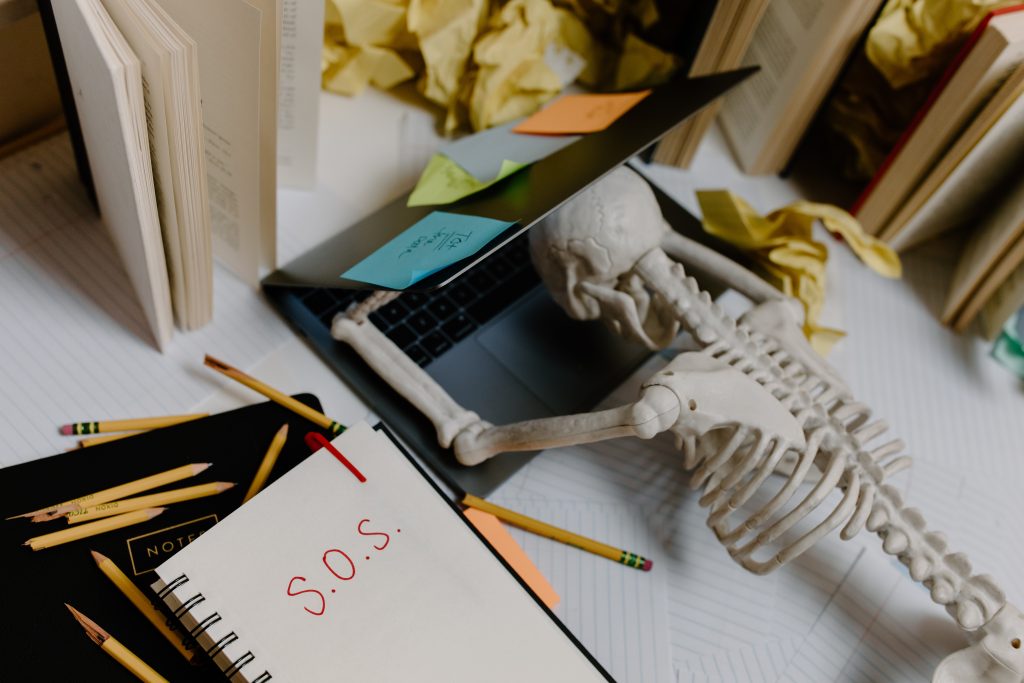 skeleton lying on laptop with SOS written on notebook due to poor mental health