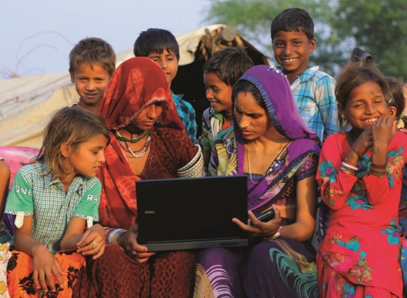 a group of indian ladies and children surrounding a laptop